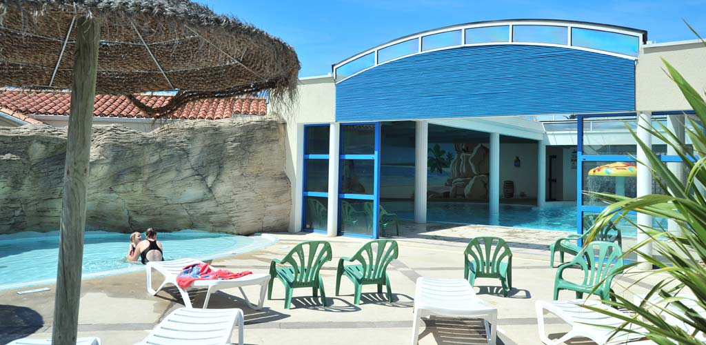 Transats devant l'entrée de la piscine couverte du camping Le Bois Tordu en Vendée