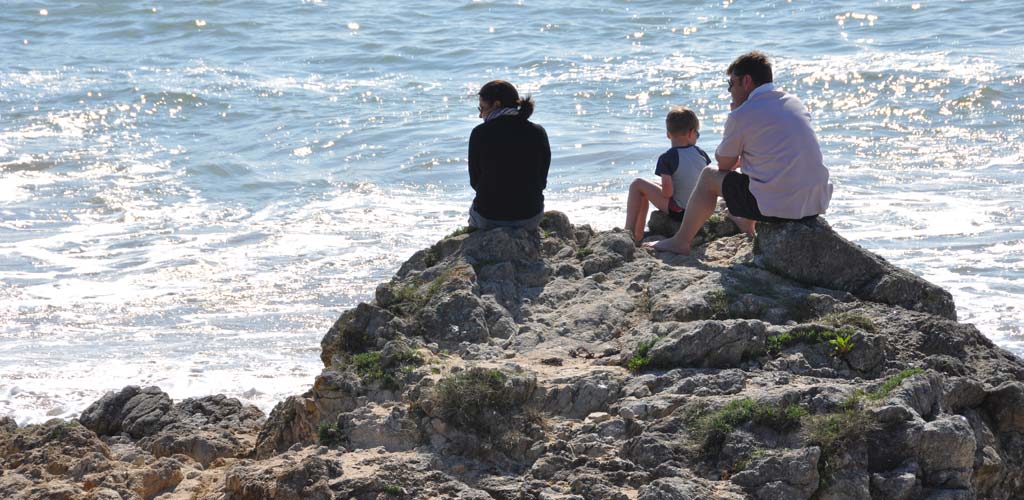 Familie van kampeerders zittend op een rots met uitzicht op zee in Saint-Hilaire-de-Riez